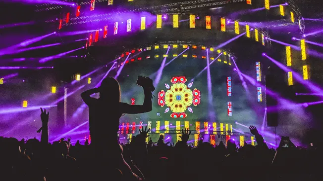 Vibrant concert stage with dynamic lighting, digital visuals, and enthusiastic crowd at a music festival or live event.