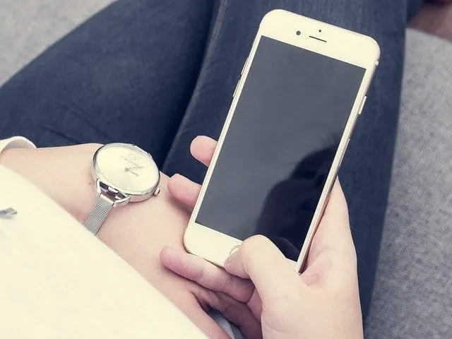 Close-up of a person holding a smartphone while sitting, focus on hand and device, modern technology, casual setting, digital