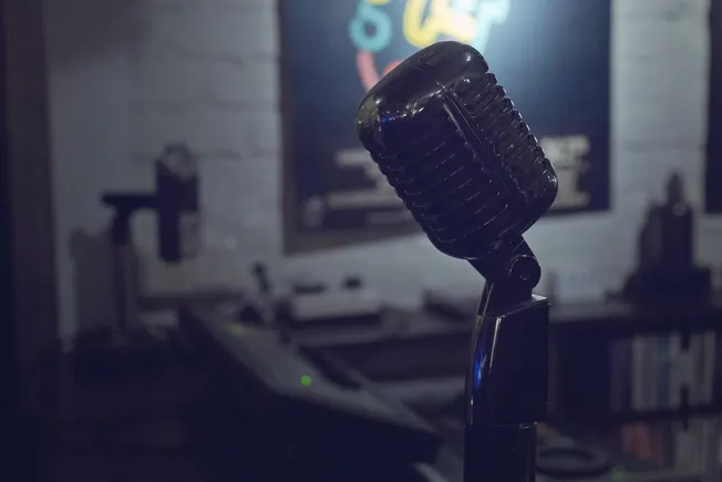 Vintage black microphone on a stand for podcasting or music recording, in a sound studio setting with audio equipment and a b