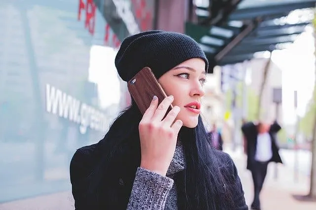A young woman talking on her mobile phone outdoors in an urban setting, stylish winter clothing, black beanie, with blurred c
