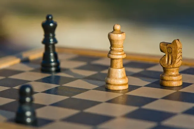 Chess game with wooden and metal pieces on a checkered board, symbolizing strategy and competition, relevant for content rela
