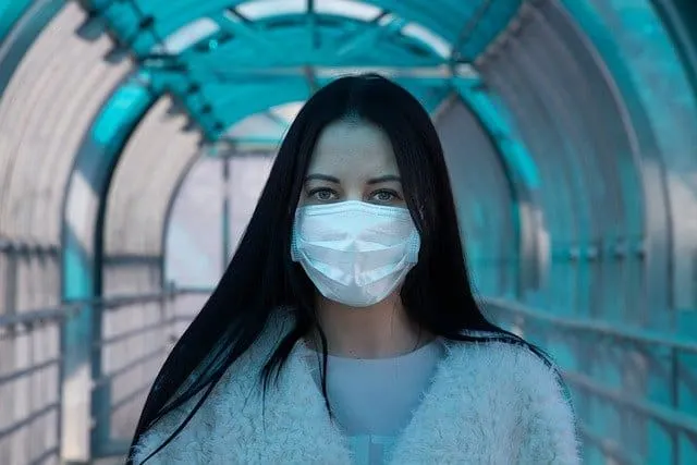 A woman with long dark hair wearing a protective face mask in a modern covered walkway, emphasizing health safety and urban e