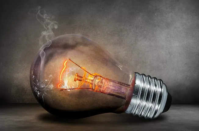Incandescent light bulb with filament glowing inside, broken glass, and smoke, symbolizing ideas, innovation, and illuminatio