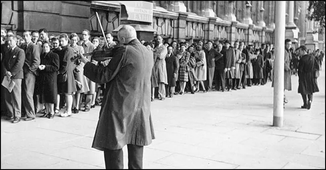 A long queue of people waiting outdoors in a city street, black and white vintage photo.