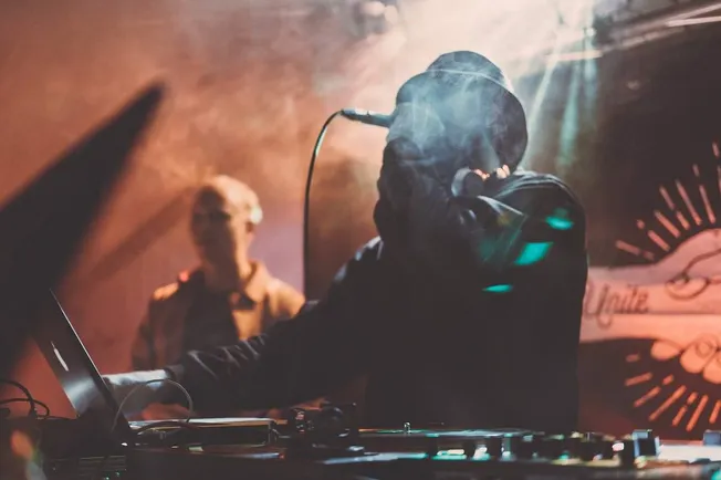 DJ performing at a live music event with turntables and computer equipment, emphasizing electronic music, nightlife entertain