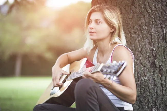 Girl playing acoustic guitar outdoors in park during sunset, relaxing and enjoying music, showcasing summer leisure, music th