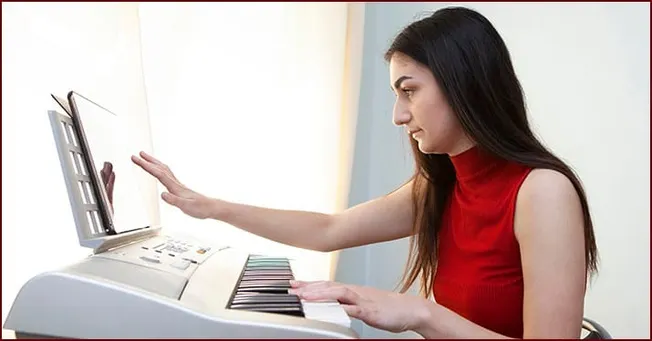 Keyboard playing woman with digital music work setup in natural light.