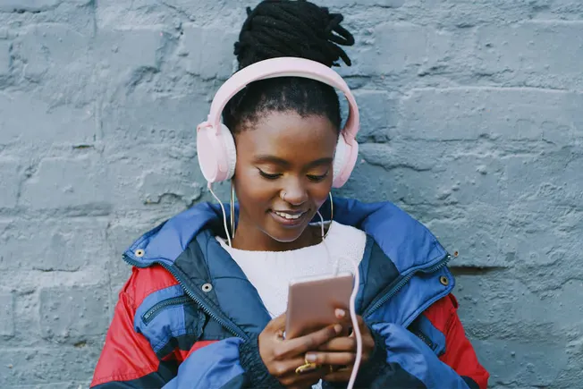 Young woman listening to music with pink headphones and smartphone against urban brick wall, enjoying music, urban lifestyle,