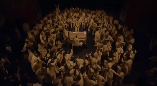 Aerial view of a live music event with a musician playing a piano surrounded by a large crowd of festival attendees, capturin