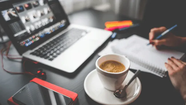 Laptop with video editing software, notebook, pen, smartphone, and coffee on a workspace – ideal for digital content creation
