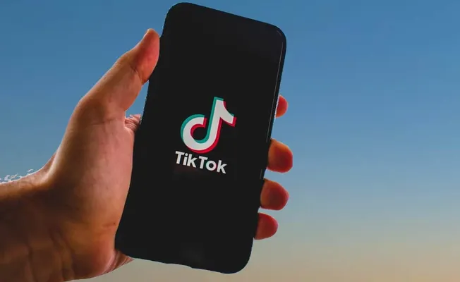 TikTok app displayed on smartphone screen against a clear blue sky, showcasing popular social media platform for short videos