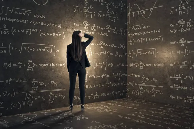 Complex mathematical equations written on a chalkboard with a woman in business attire analyzing data in a modern classroom.
