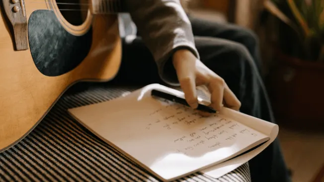 Guitarist taking notes with a pen on a notepad near an acoustic guitar, music songwriting, musicians brainstorming, creative