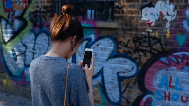 Woman using smartphone in front of graffiti wall with colorful street art and murals, urban scene, girl browsing mobile devic