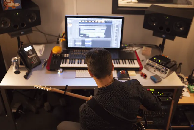 Professional music producer working in a modern home studio with digital audio workstation, mixing equipment, and musical ins