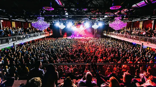 Bright concert crowd enjoying a live music event with vibrant stage lighting and elaborate chandeliers, emphasizing the inter