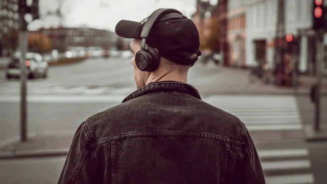 Headphones on man walking across city street, urban environment, music or podcast listening, street scene, trendy city lifest