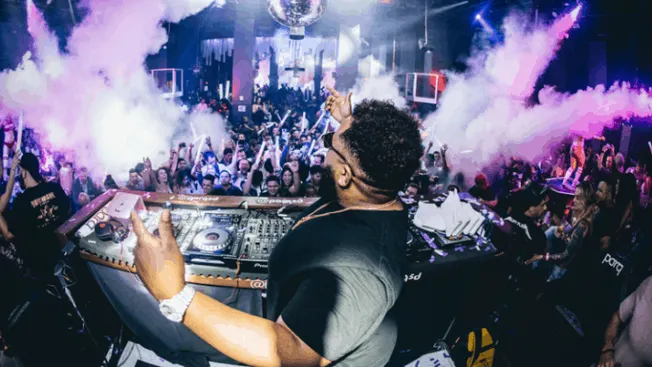 DJ performing at a vibrant nightclub with an energetic crowd, colorful lighting, and dynamic smoke effects, capturing the ess