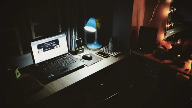 Laptop workspace at night with desk lamp, smartphone, and headphones, showcasing a creative home office setup ideal for digit