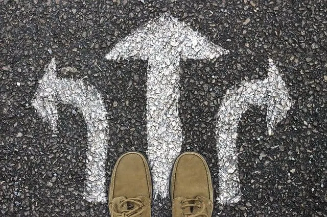 Uncertain path options with directional arrows painted on asphalt, viewed from a person's feet, symbolizing decision making a