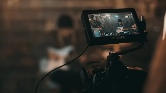 Professional music video recording setup with camera capturing live band performance in a studio. Advanced filming equipment