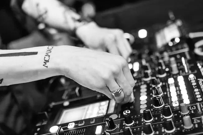 DJ mixing a track using a professional DJ controller with illuminated buttons, focusing on music production, DJ performance,