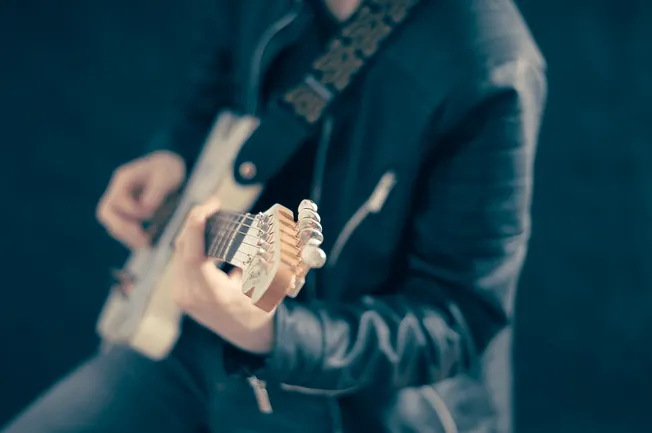 Close-up of a person playing electric guitar, focusing on the guitar neck and hand, with a blurred background, showcasing mus