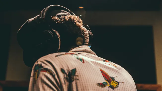 Headphones wearer in a recording studio wearing a floral and butterfly print shirt, focused on music production, representing