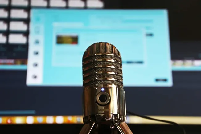 Microscope microphone in front of computer screen with music editing software, representing audio recording, podcasting, and