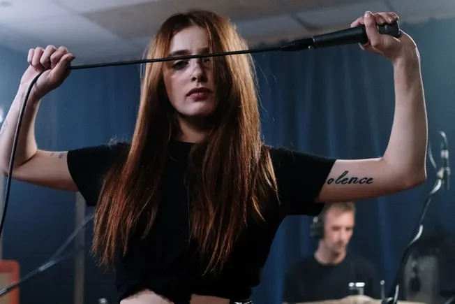 Female singer holding microphone cable, performing in a recording studio or live music venue, with a deep focus on music perf