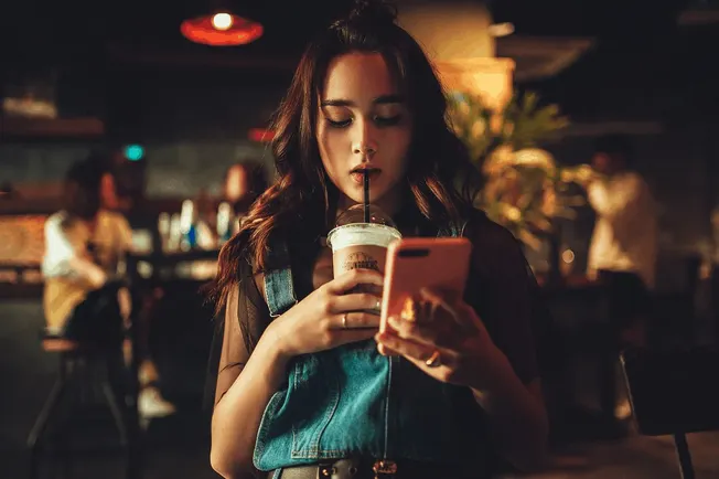 Young woman drinking soda while using smartphone in a cozy cafe, social media, digital content, trendy lifestyle, casual fash