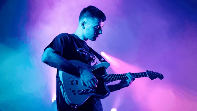 Electric guitar player performing on stage with colorful lighting.