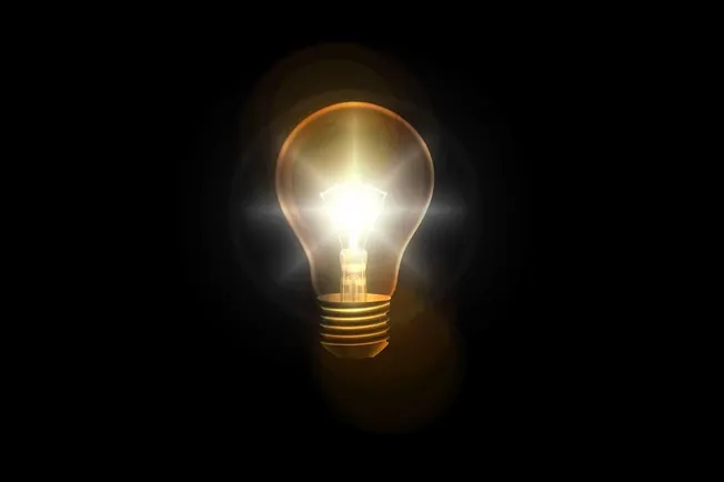 Illuminated incandescent light bulb glowing in darkness symbolizing ideas and innovation.