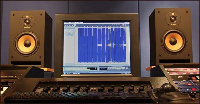 Studio music production equipment with computer monitor displaying audio editing software, professional sound mixing setup fo