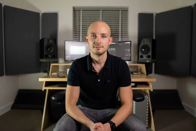 Bald man in music studio with professional sound equipment, mixing consoles, studio monitors, and acoustic panels, creating a