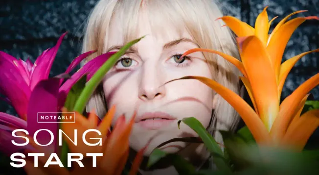 Bright blonde woman surrounded by vibrant tropical flowers, emphasizing music and pop culture themes, with a focus on fresh,