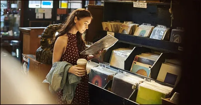 Woman browsing vinyl records at a music store or record shop with a hot beverage in hand, exploring music collections for art