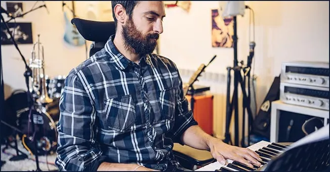 Music producer working at a keyboard in a home studio with musical instruments and equipment for music production and songwri