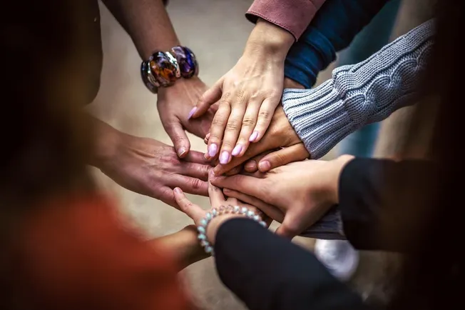 Hands joined together in a circle, symbolizing unity, teamwork, and collaboration in a diverse group, representing community