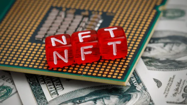 NFT blockchain digital assets concept with red dice spelling NFT on a circuit board and US dollar bills in the background.