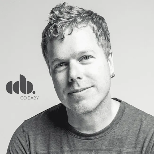 Close-up photo of a young man with curly hair, wearing a casual t-shirt, smiling confidently. Black and white portrait emphas