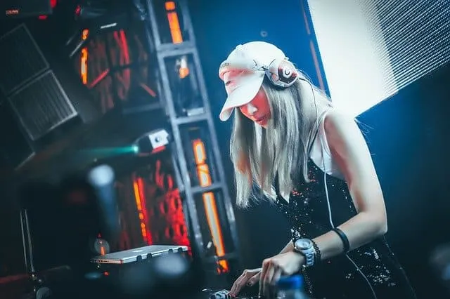 HD DJ performing at a music event with turntables and professional sound equipment, wearing headphones and a hat, illuminated