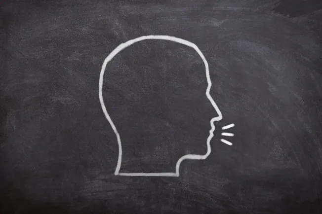 Silhouette of a person's head drawn with white chalk on a blackboard, with lines indicating speaking or communication.