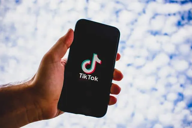 TikTok logo displayed on a smartphone held in hand against a bright sky background, emphasizing social media marketing, digit