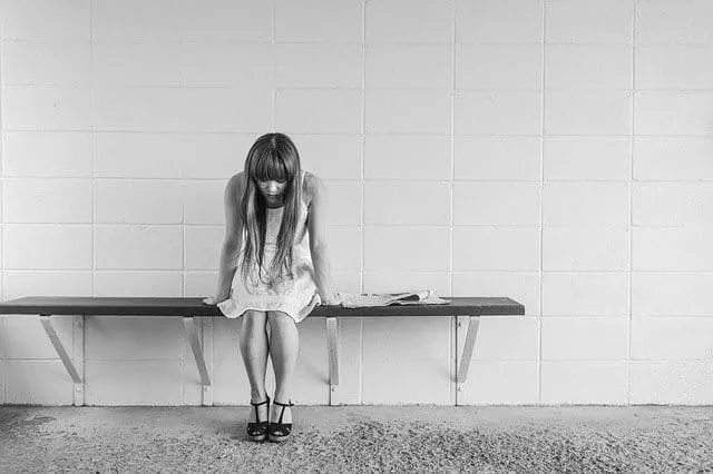 Waiting woman sitting alone on a bench with a wall background, representing loneliness or contemplation.