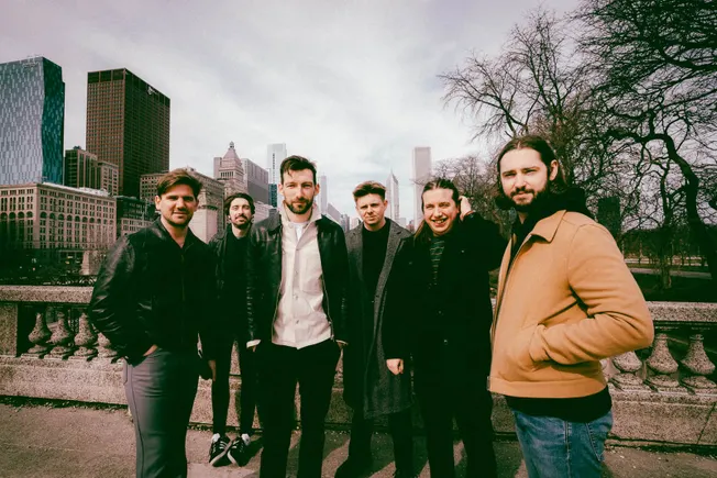 Urban skyline with a group of five casually dressed young adults standing outdoors in a city park, capturing a trendy and div