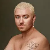 Blonde-haired individual with a tattoo on their shoulder, looking confidently at the camera for a music or fashion-related ph