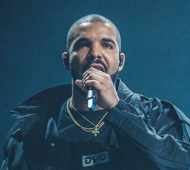 Boy holding a microphone performing on stage at a music event, dressed in dark clothing with gold chains, youtube logo, and w