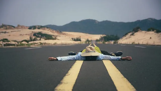 Dead body lays on a deserted road with mountains in the background, symbolizing exhaustion or burnout in the music industry o