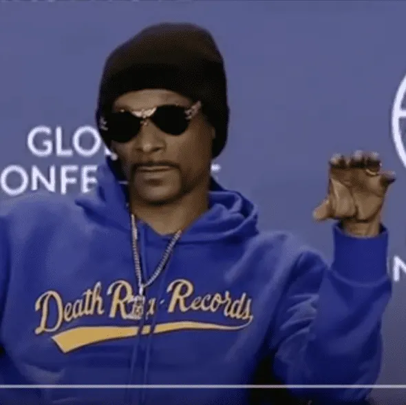DJ Snake wearing sunglasses and a blue Death Row Records hoodie at a music industry event.